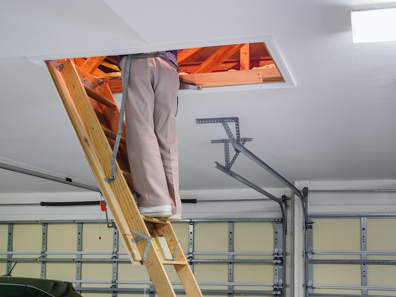 Man inspecting garage attic. Male homeowner climbing wooden pull down attic ladder stairs.