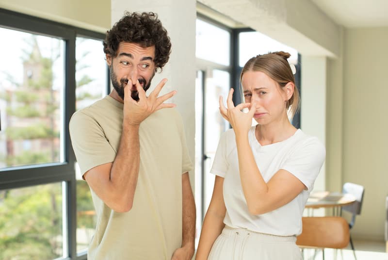 young adult couple feeling disgusted, holding nose to avoid smelling a foul and unpleasant stench