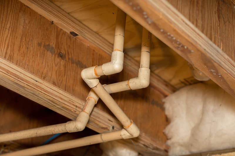 Old PVC plastic water supply pipes installed under house in crawlspace. Hot and cold water plumbing system for bathroom sink and shower