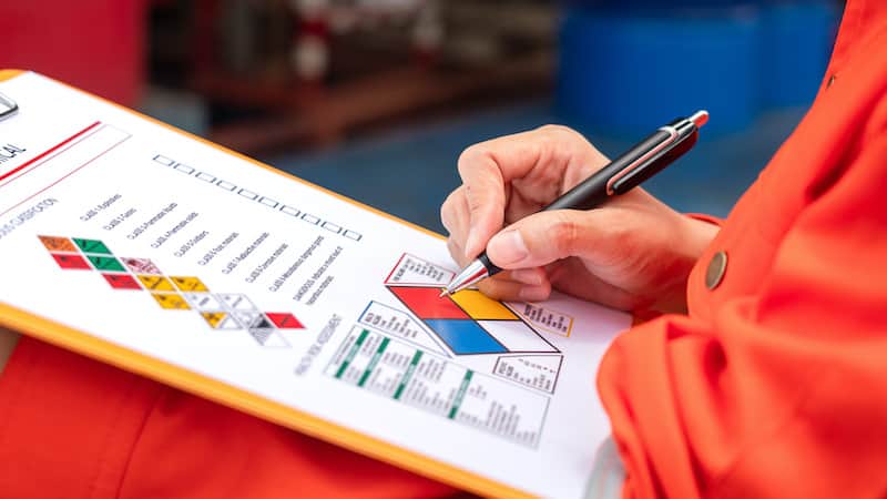 A safety engineer is using pen to rating the health risk assessment level of chemical hazardous material in the paperwork form. Industrial safety working scene, close-up and selecitve focus.