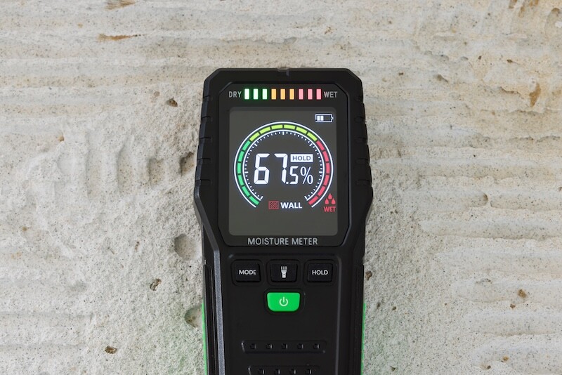Moisture detector (moisture testing meter) on a concrete floor, reading high moisture content. UK home interior