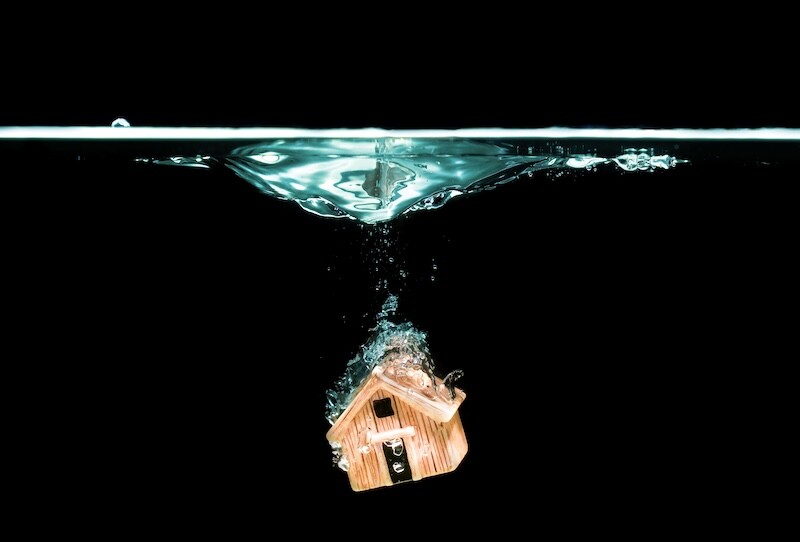 Toy house model submerged in water on black. Home insurance related concept.