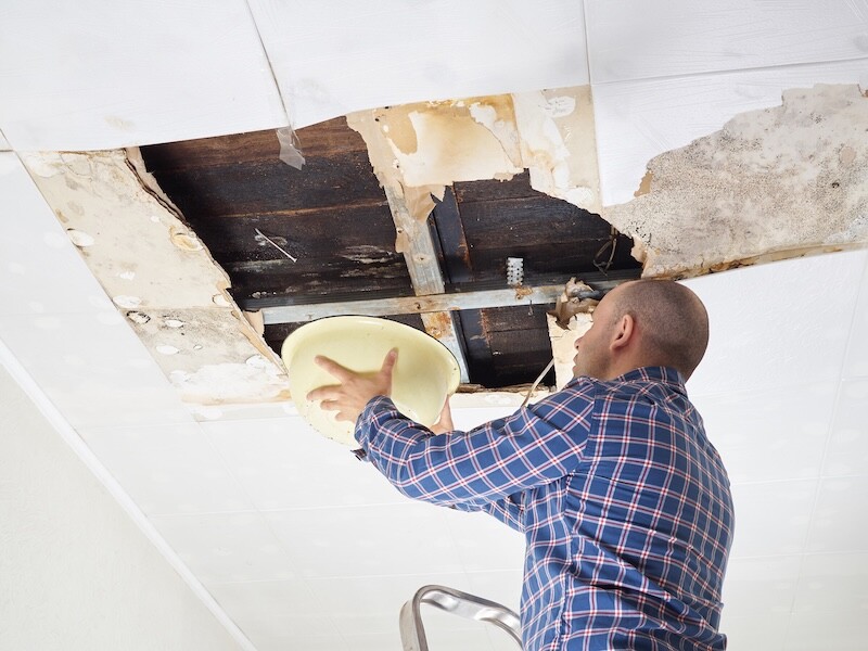 Man Collecting Water In basin From Ceiling. Ceiling panels damaged  huge hole in roof from rainwater leakage.Water damaged ceiling .