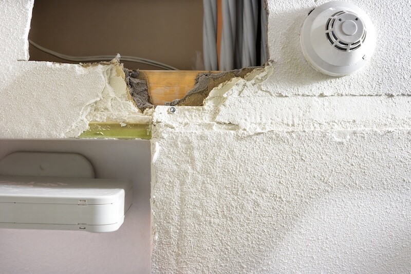 Ceiling with water damage from water leak. Active leak investigation of ceiling with holes cut out by plumber, yellow wet moisture, peeled off drywall, cables and smoke detector. Selective focus.