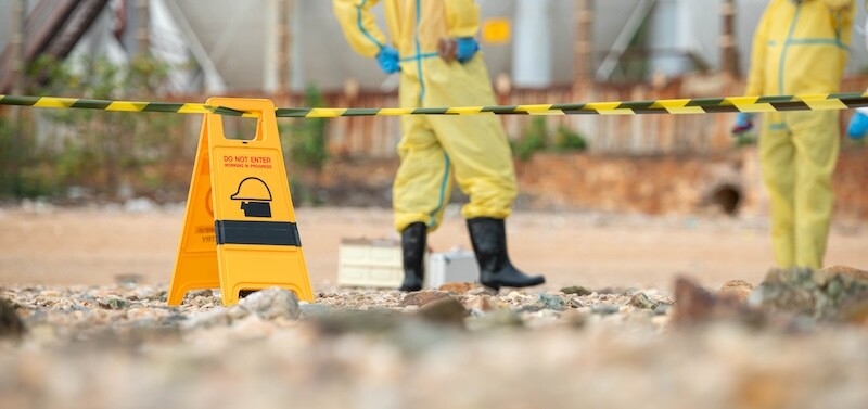 Warning sign and restricted area barrier at hazardous environmental cleanup site with hazmat workers in background