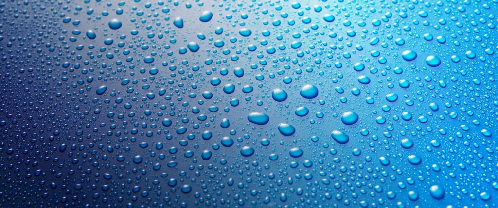 Panoramic banner of water drops from rain, dew or splashing on blue metal surface forming an abstract random background pattern