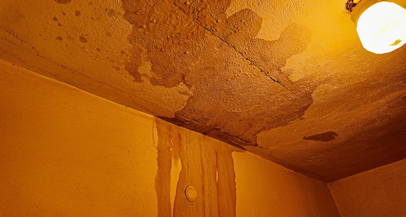 Water damage and stains on a textured ceiling and wall with a light fixture. Visible signs of water infiltration and damage are evident on the textured ceiling and adjacent wall, with staining and cracks indicating a problem.