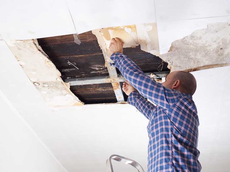 Man repairing collapsed ceiling. Ceiling panels damaged  huge hole in roof from rainwater leakage.Water damaged ceiling .