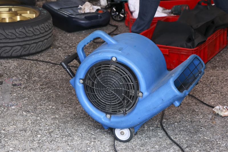 Powerful blue industrial air mover fan sits on concrete floor in garage. This portable ventilation and drying equipment used for professional work in workshop