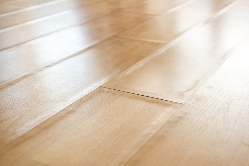 Swollen laminate flooring from flood or water damage, perspective view. Close up of light beige swollen laminate boards with buckling edge pieces. Floor damage texture. Selective focus in center.