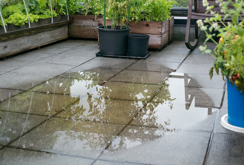 Patio drain clogged and flooded after heavy rain. Overflown drainage causing to pool large amount of water on tiles. Unclog the drain from mud or dirt or plumber has to snake pipe. Selective focus.